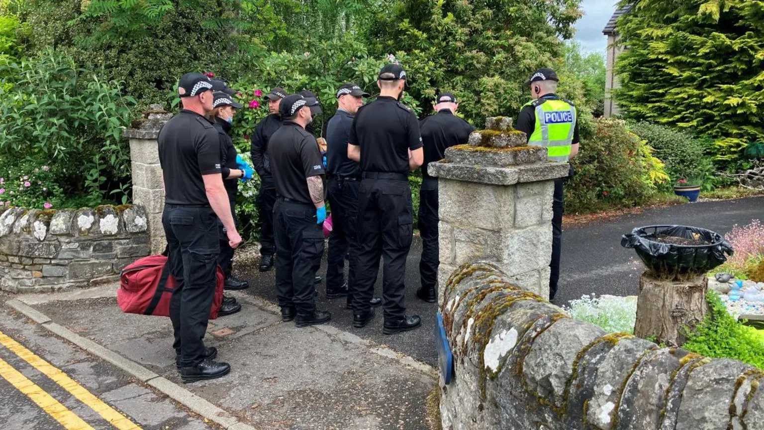 Eight police officers stand at the entrance to a property