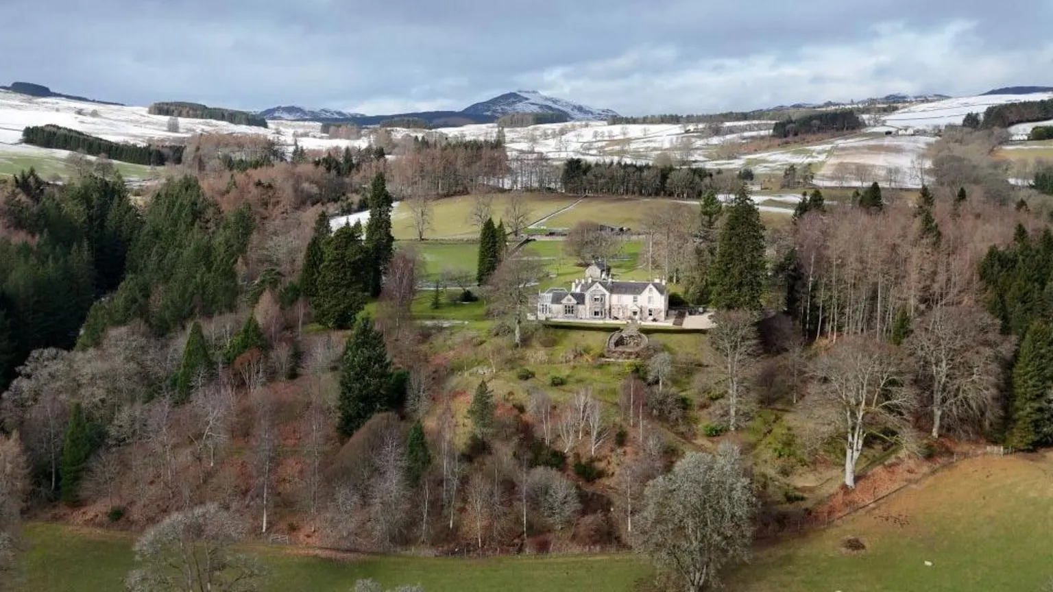 Drone footage of the Edradynate Estate set in lush green countryside with snow-covered hills visible in the distance.