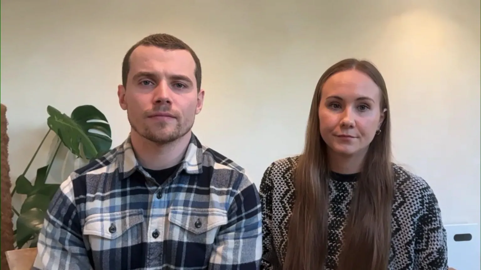 Jonathan and Robyn Davis sit next to one another, in front of a white wall, looking into the camera. Jonathan has short dark hair, and is wearing a dark blue and white patterned shirt. Robyn has long brown hair and is wearing a black and white patterned jumper
