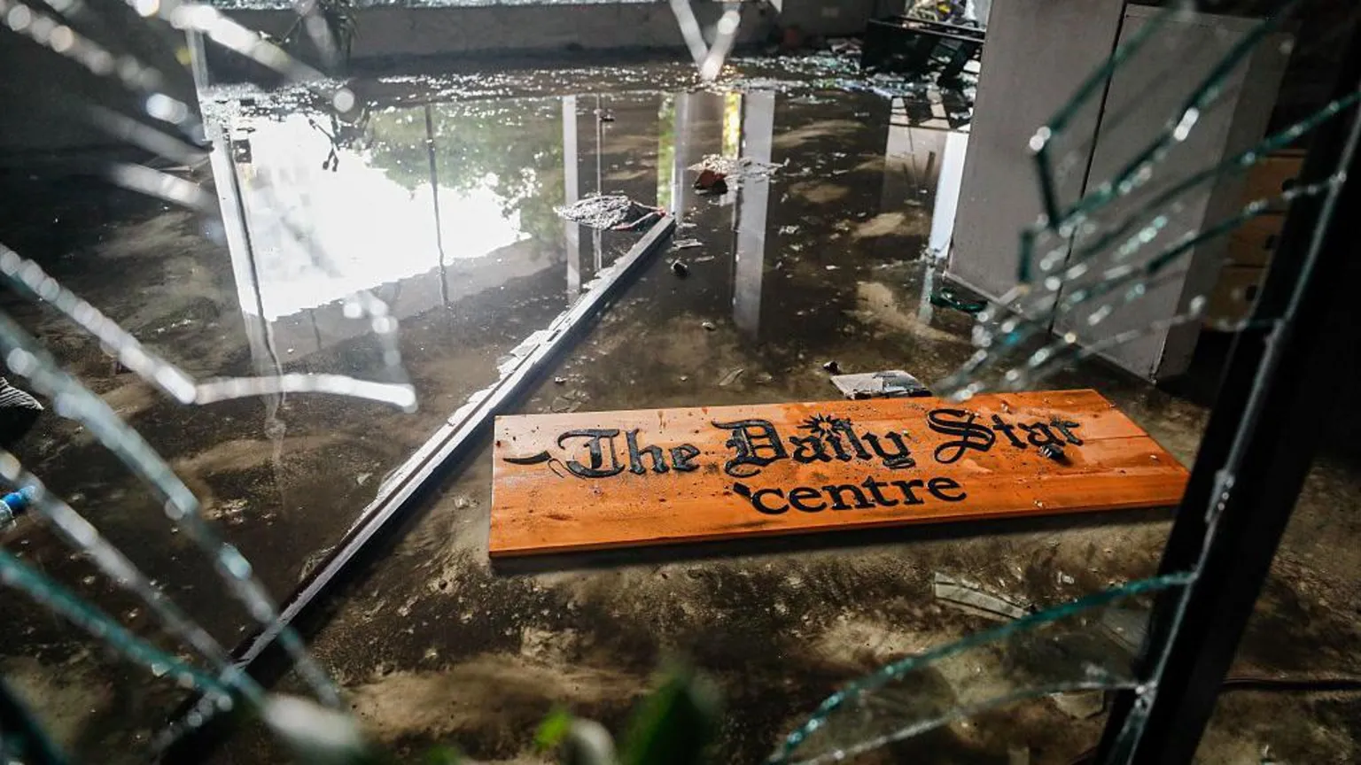 NurPhoto via Attackers vandalised and torched The Daily Star office, causing extensive damage. A shattered sign lies amid broken glass at reception.