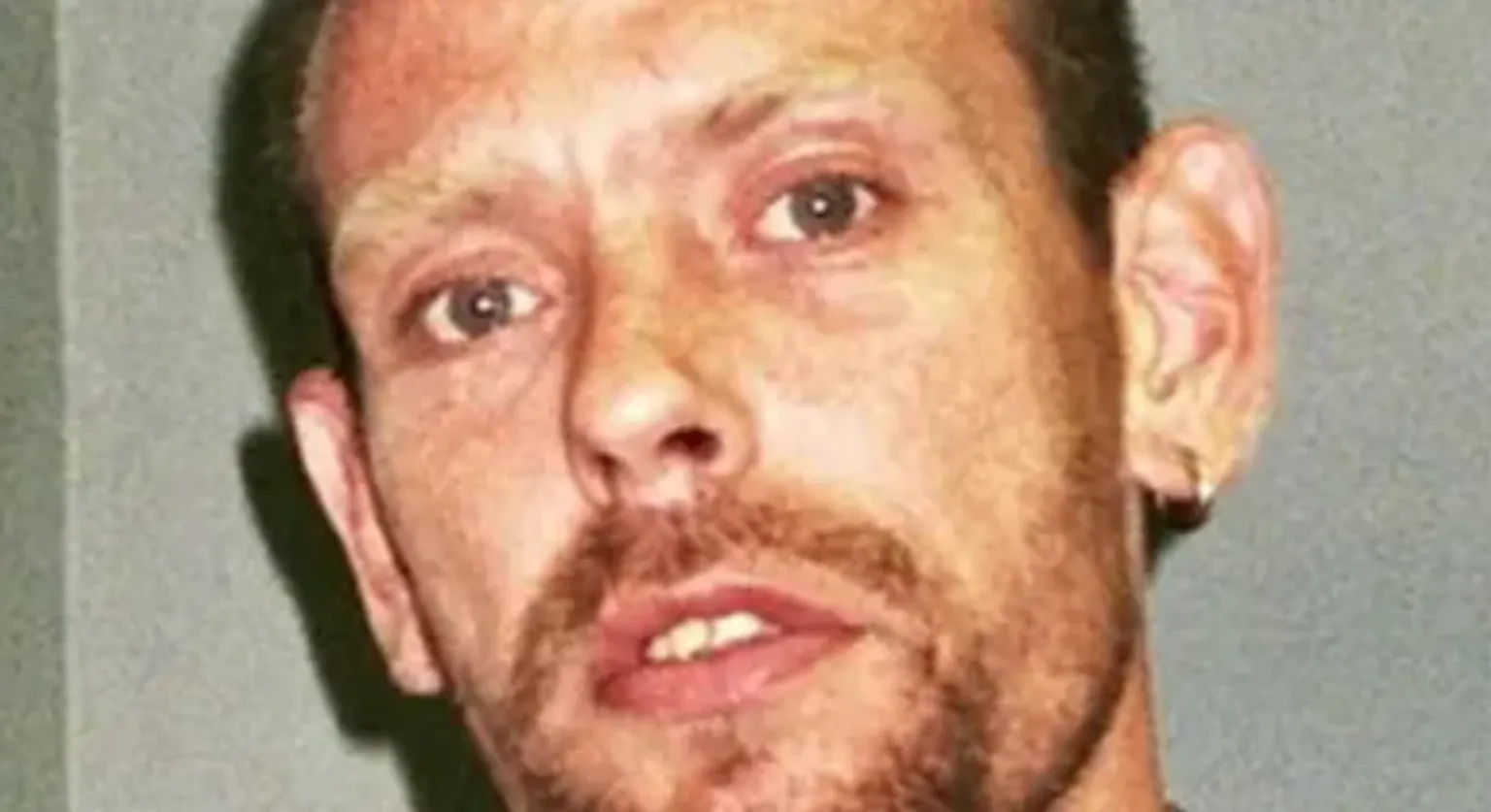 Suffolk Police A close-up image of Paul Clarke. He is looking directly into the camera and standing in front of a grey wall.