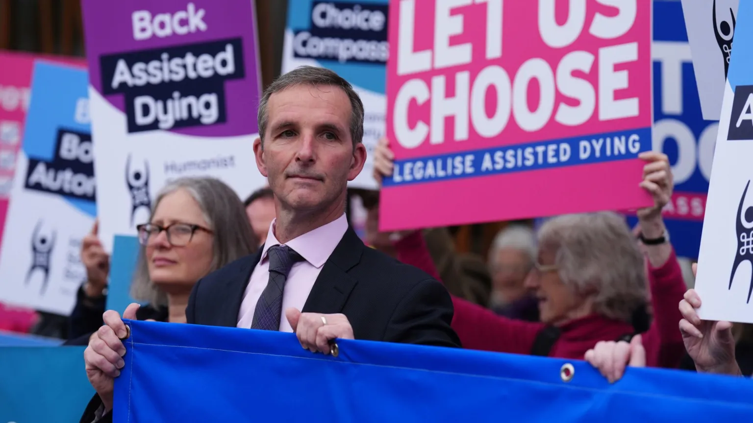Liam McArthur stands alongside people holding signs in favour of his assisted dying bill outside the Scottish Parliament