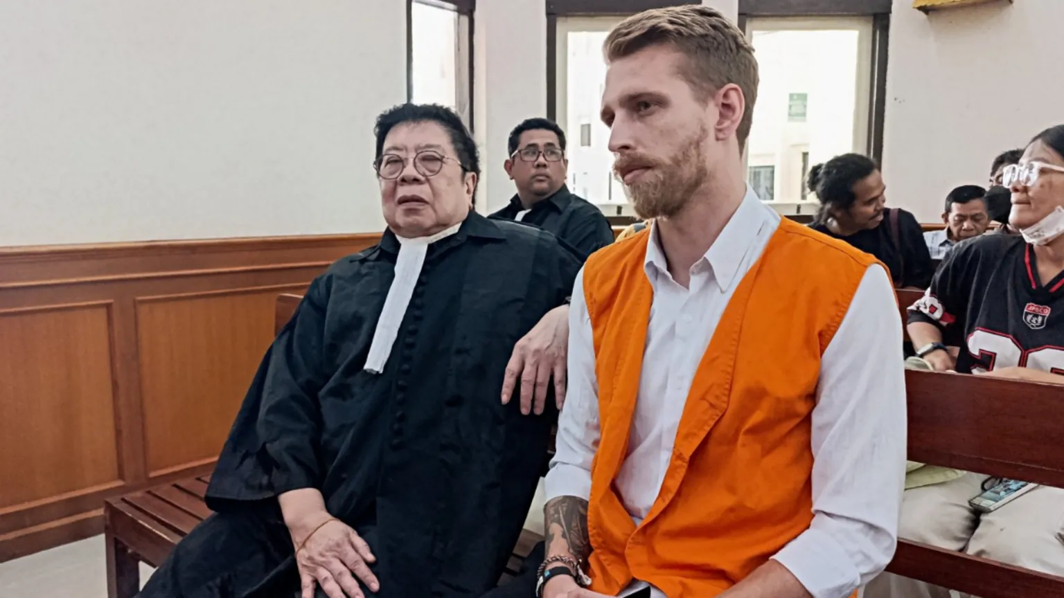  Kial Robinson sits wearing a white shirt and an orange waist coast with his lawyer in a courtroom as they wait for the verdict in Robinson's trial on charges of alleged cocaine smuggling, at the Denpasar District Court in Bali, Indonesia