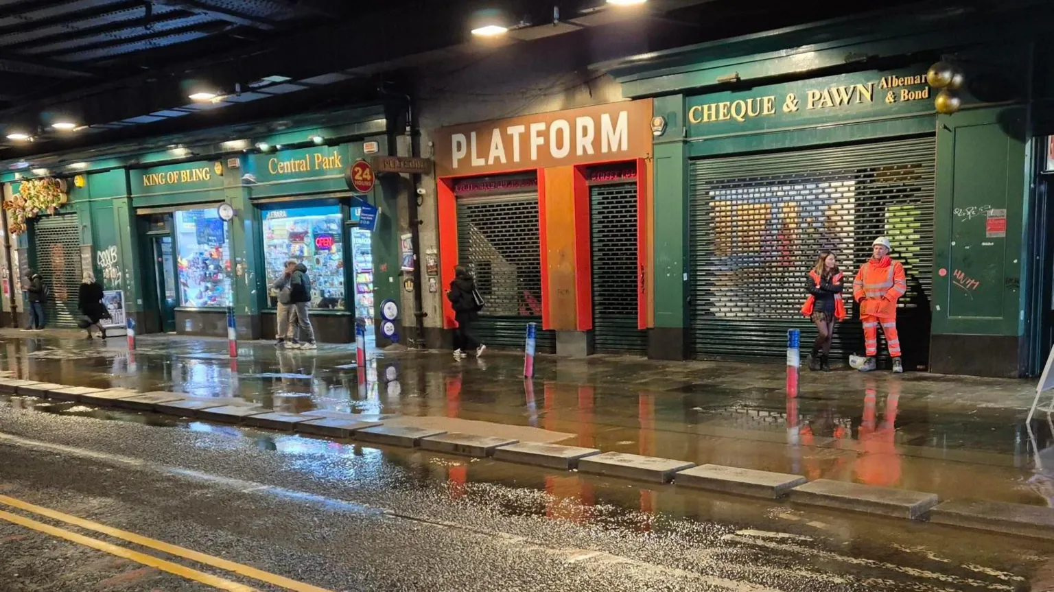 Shop entrances painted green and red on Argyle Street in Glasgow. There is flooding on the pavement and people walking along the street.
