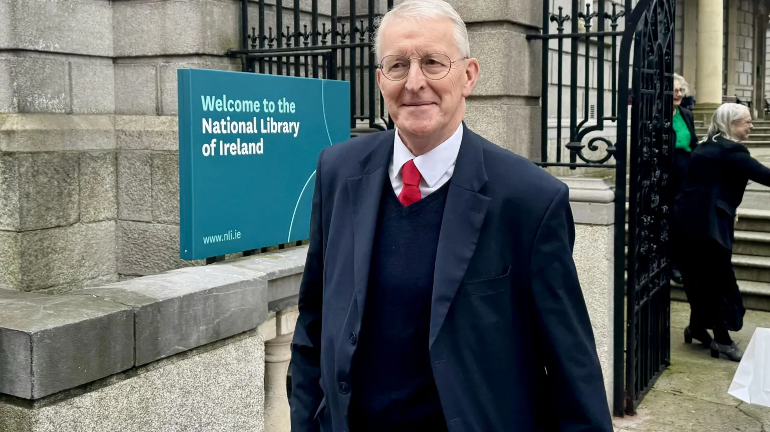  A white-haired man in a suit walks across the street. 