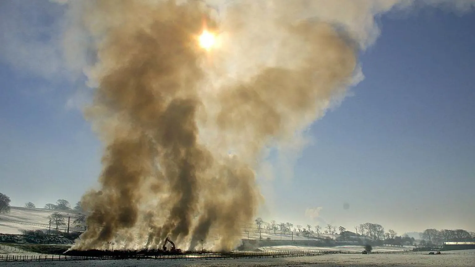  Smoke rises from some 300 cattle and 400 sheep infected with foot-and-mouth disease being incinerated on a farm in Scotland in March 2001. The smoke dominates the photo as it rises into the cloudless sky, with frosty fields around it. 