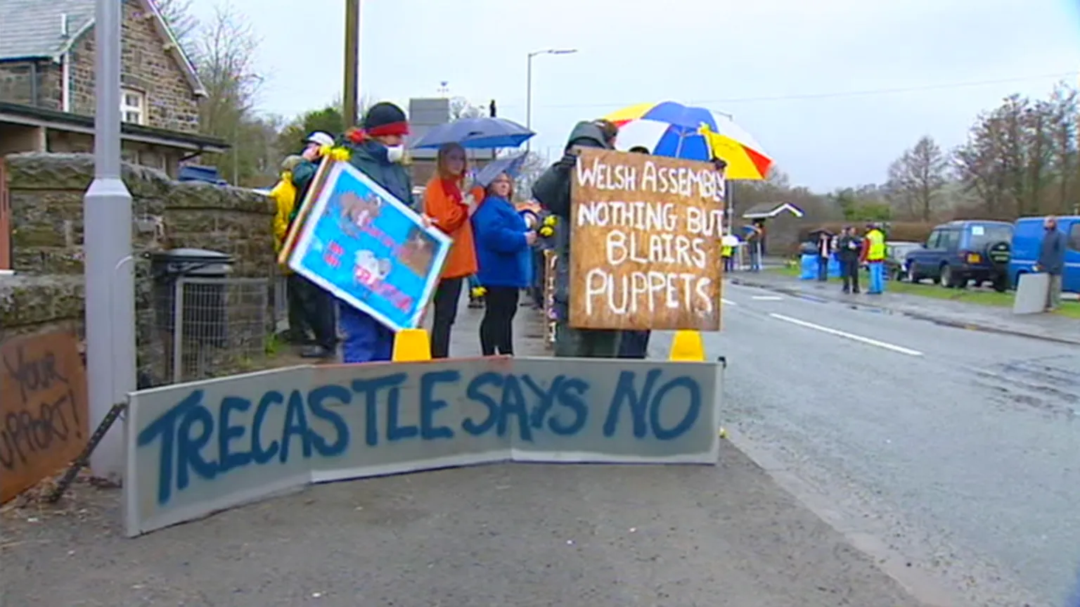 Protesters in Trecastle holding umbrellas and placards saying 