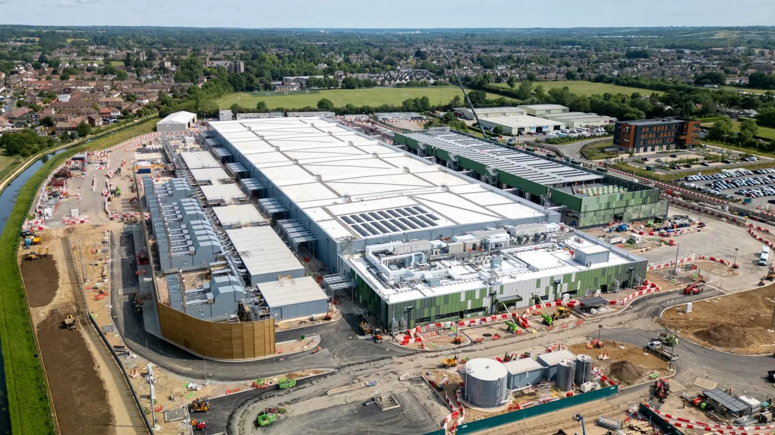  A large white data centre building under construction in Hertfordshire, surrounded by green land, a river and housing estates further afield.