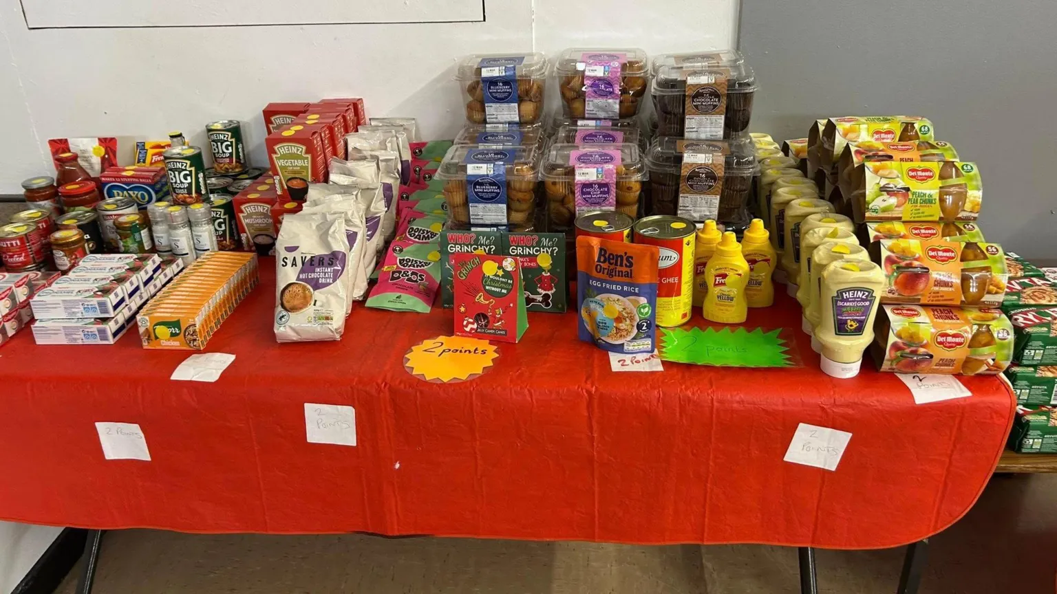 Daventry Community Larder A table full of food items, all in rows, sitting on a red tablecloth. 