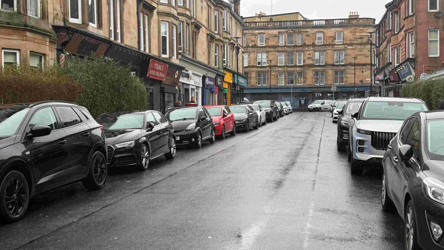 A busy street with parked cars and rows of shops in Glasgow's south side.