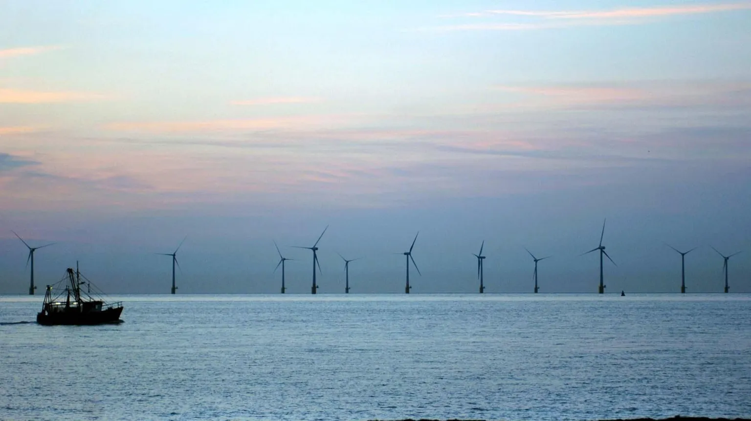  Wind turbines in the sea on the horizon. A trawler is moving from left to right in the foreground.