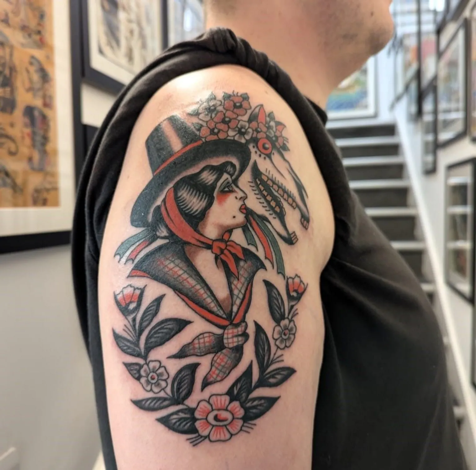 Chris Collins A traditional style tattoo on a man's upper arm. It features a woman in traditional Welsh clothing next to a Mari Lwyd - a horse skull decorated with flowers.
