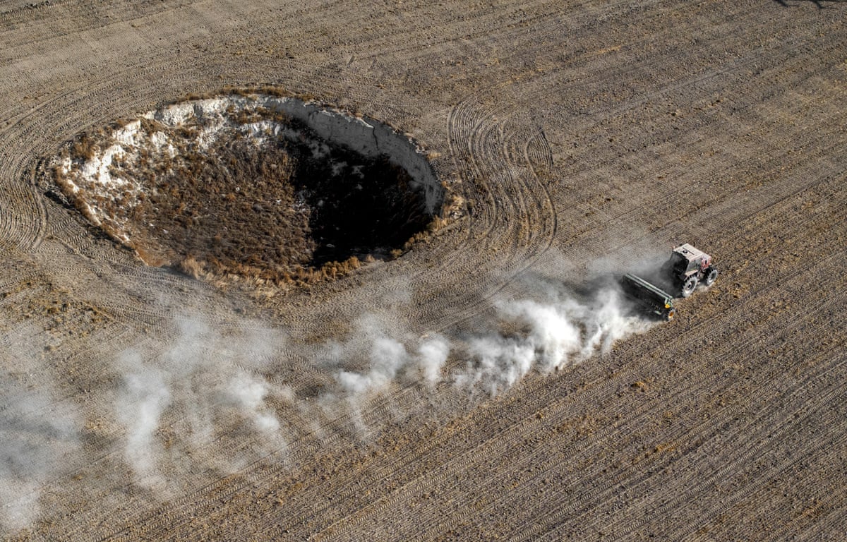 A tractor ploughing a field near a large sinkhole