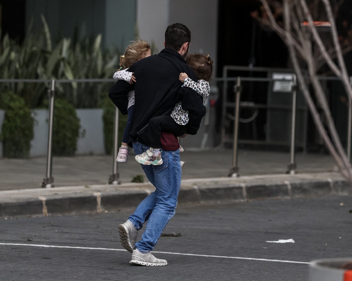 A man carries two children as he runs to take shelter after sirens sounded in Tel Aviv.