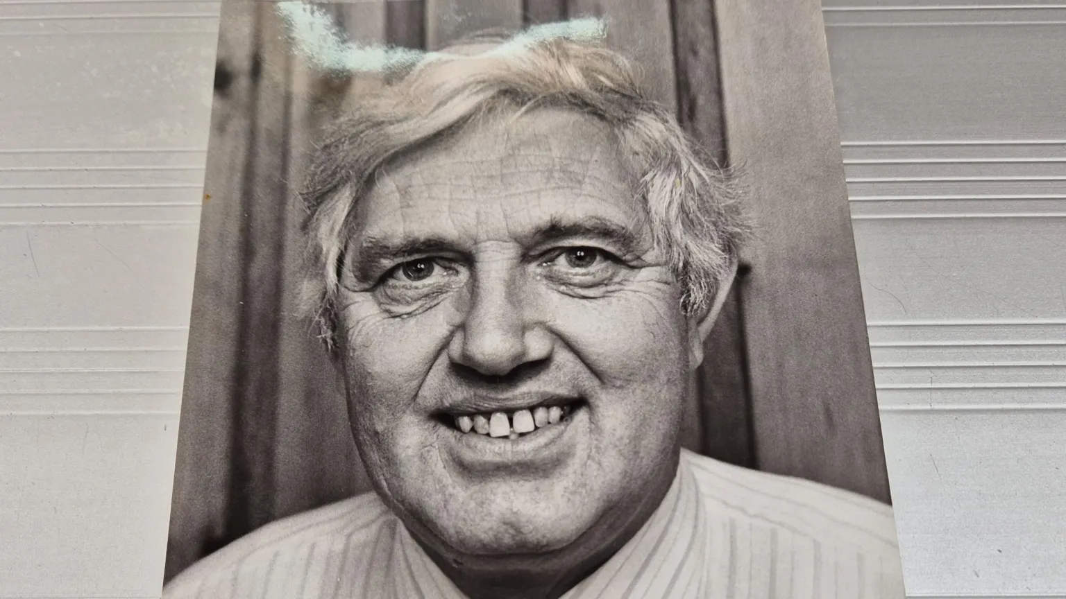 James Baillie A black and white photo cut out showing a man with white hair, smiling into the camera.