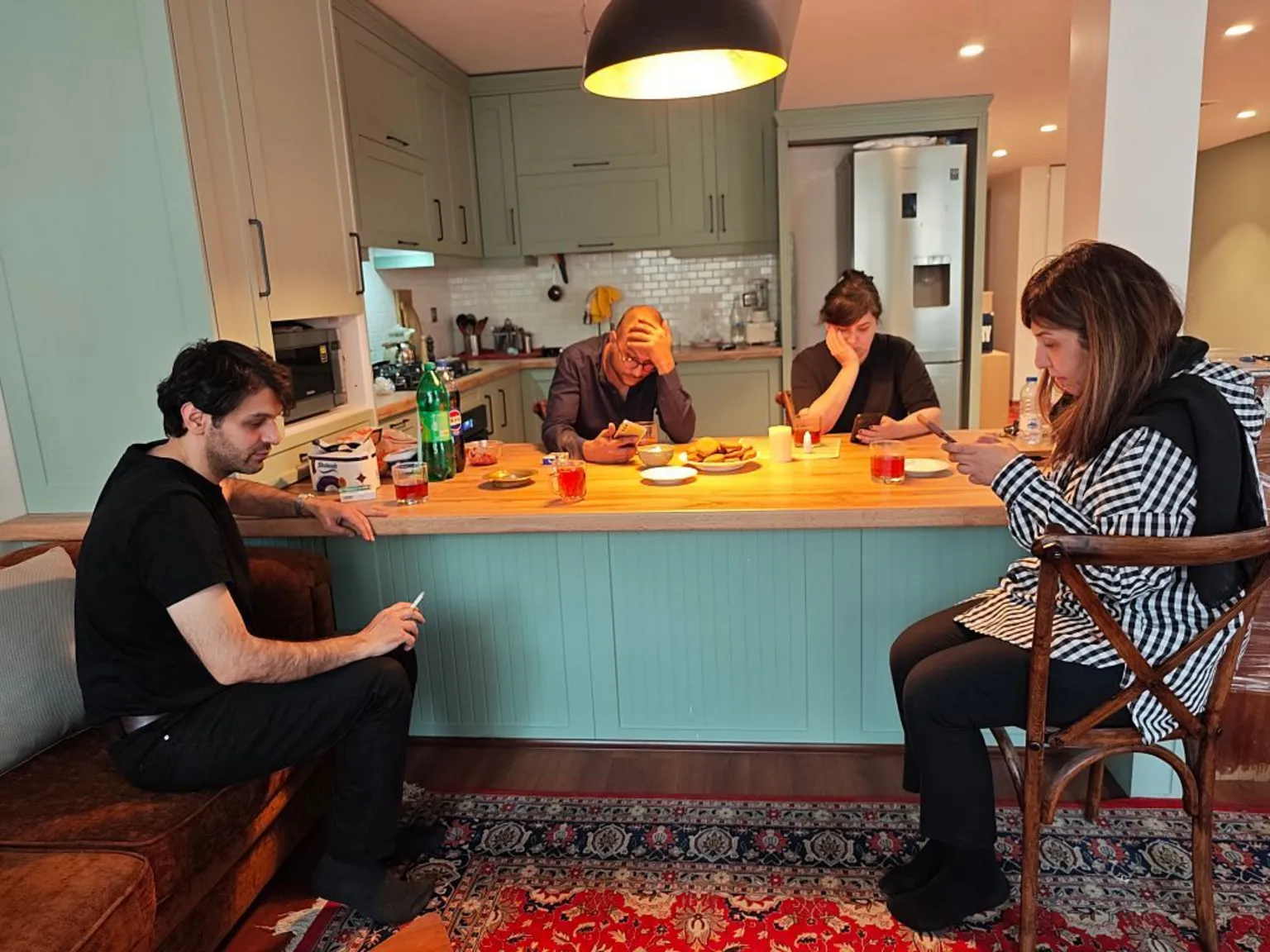  Two men and two woman sit around a kitchen table in a Tehran apartment checking their phones