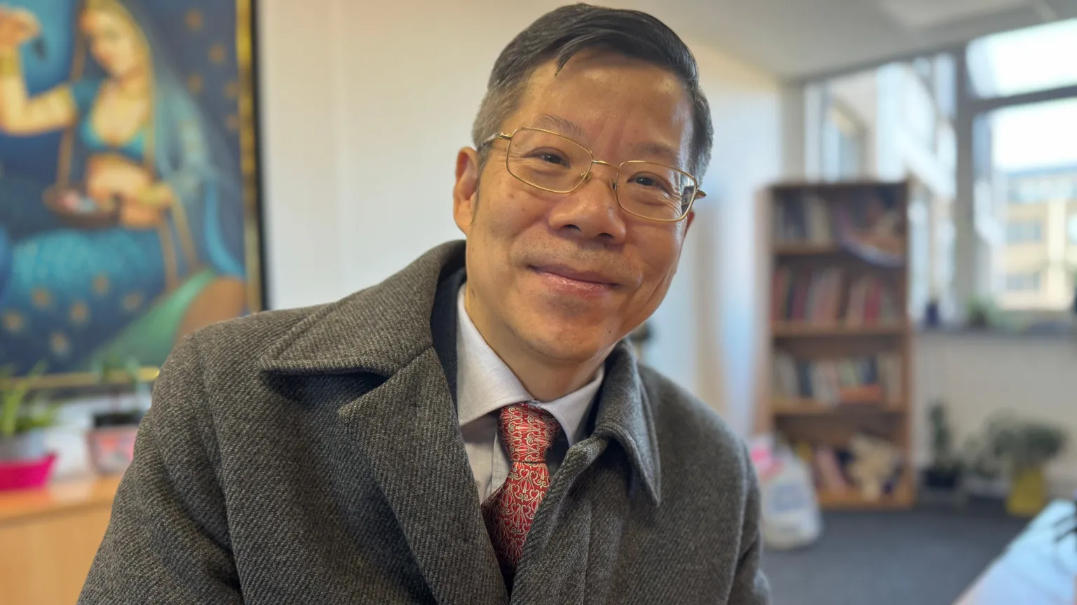 A man looking at the camera smiling, he has dark hair and glasses