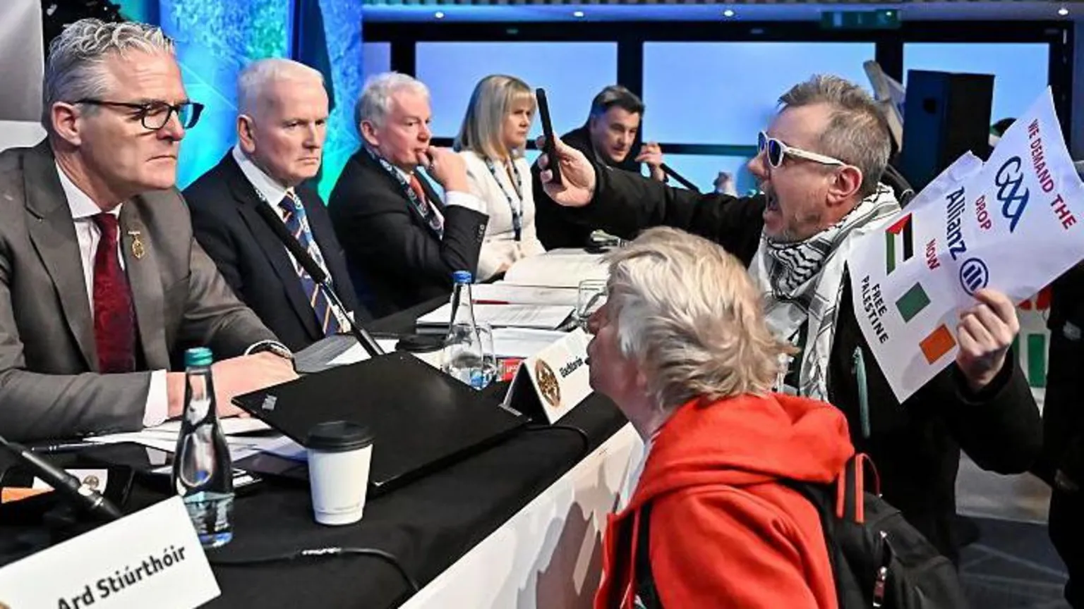  Protestors talking to a panel while holding a sign and recording it with their phone.