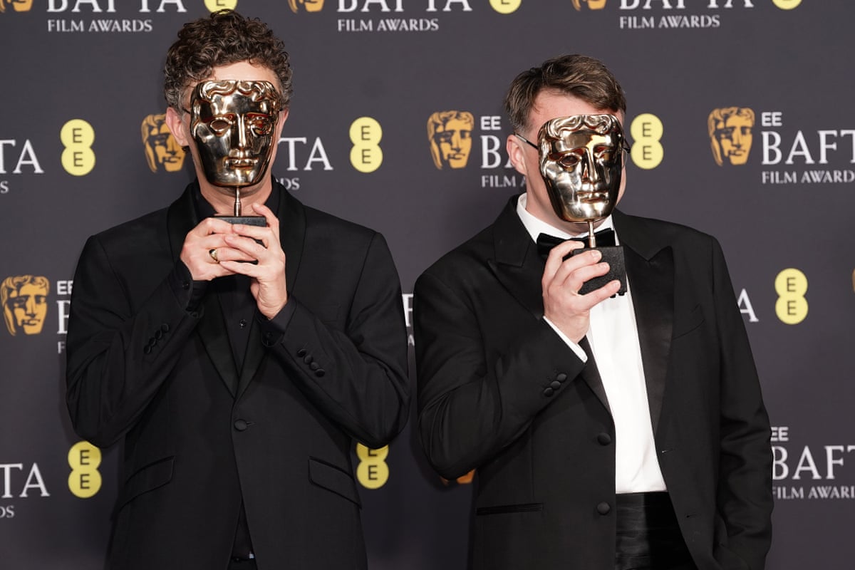 The two film-makers holding the Bafta award masks over their faces