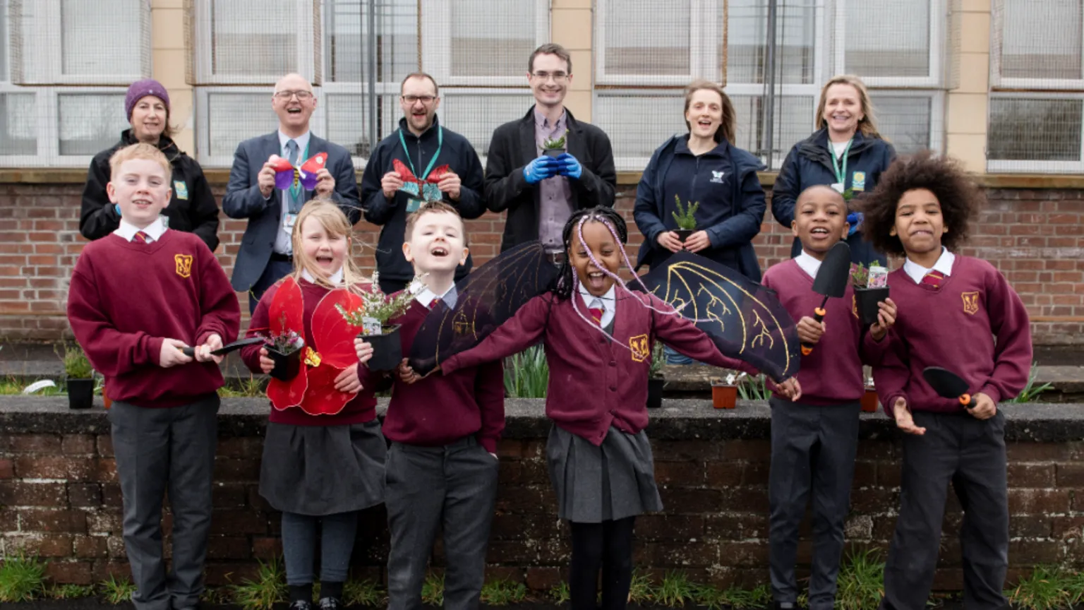 Julie Broadfoot A group of schoolchildren standing in front of a group of adults holding plants with excited expressions