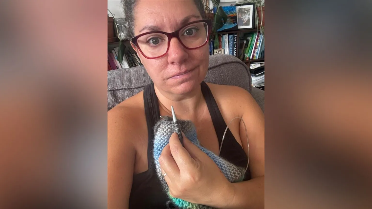 Mairead Morgan Mairead is wearing glasses and knitting. She is sitting on a sofa with a bookcase behind her.