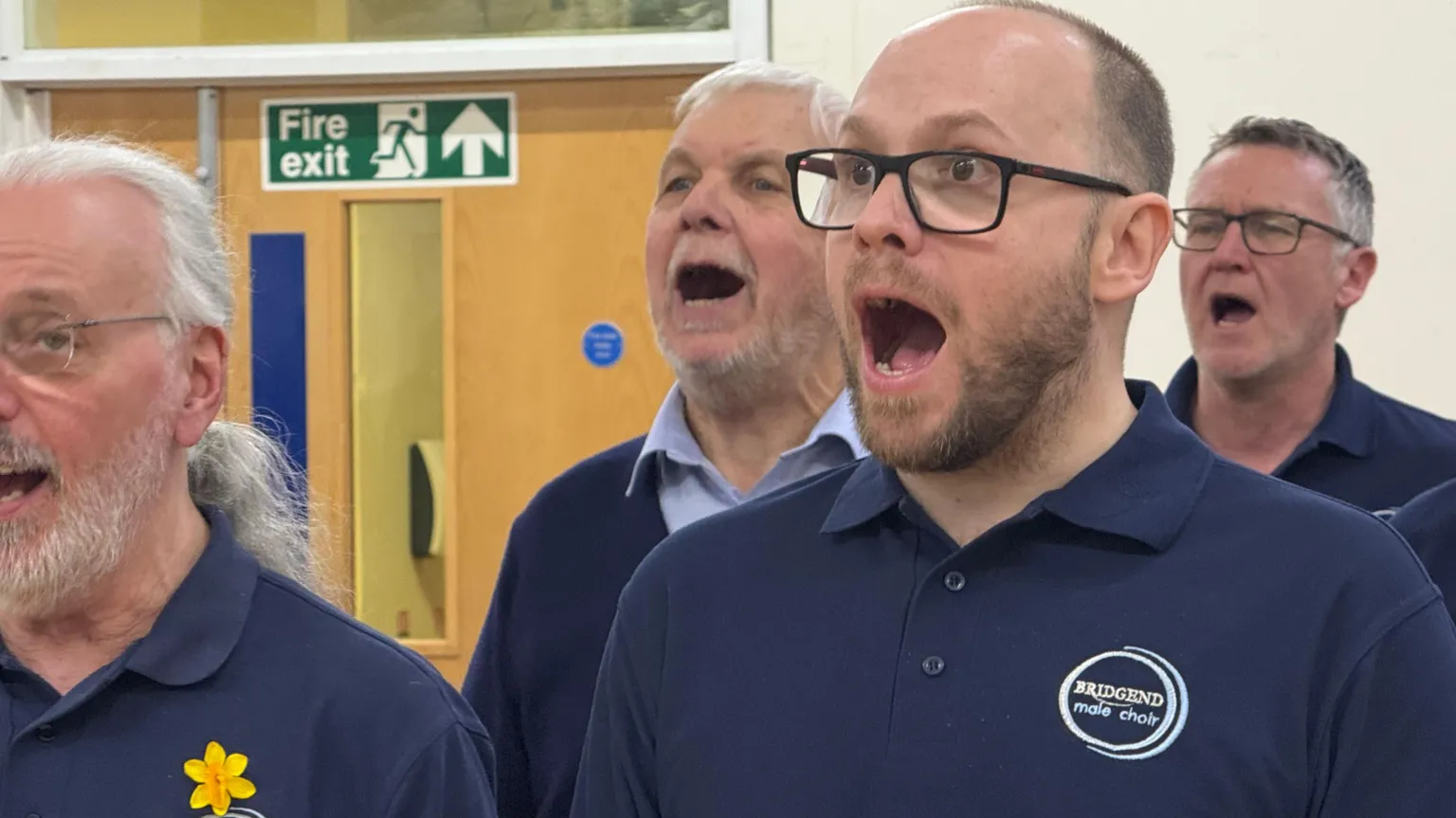 Four choristers are pictured in the choirs navy blue choir polo shirts and singing in rehearsal. 