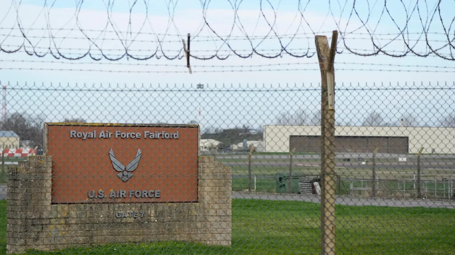  The entrance of RAF Fairford. There is a brick wall and a brown sign that reads 