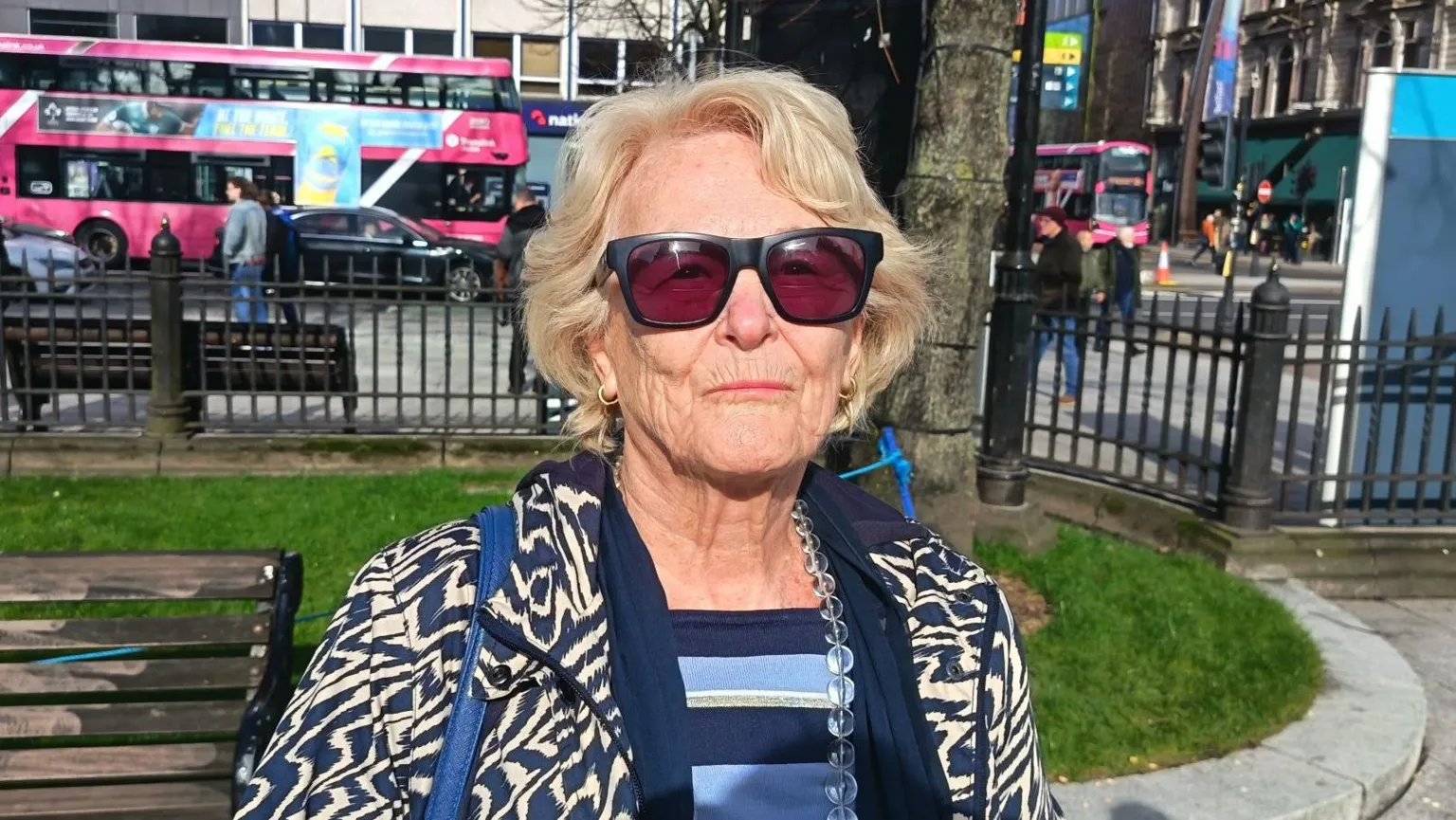Barbara Foster is an older woman with light blond hair and sunglasses. She is standing in Belfast City Hall