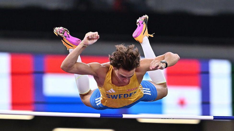 Armand Duplantis in action during the men's pole vault final on day three of the World Athletics Championships Tokyo. He is several metres above the ground with his arms and legs raised at the moment he attempts to clear the bar.