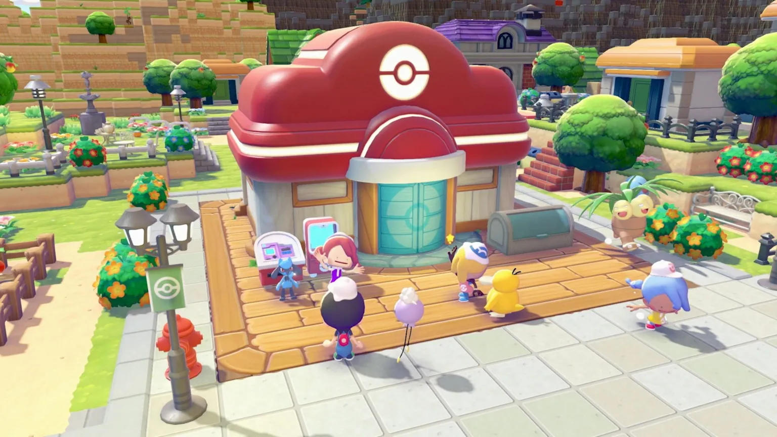 Pokémon Screenshot from Pokopia shows a small building with a red roof as various Pokémon congregate outside. They're all facing Ditto, moving its arms expressively as it smiles at them. The building is surrounded by trees, grass and fences.