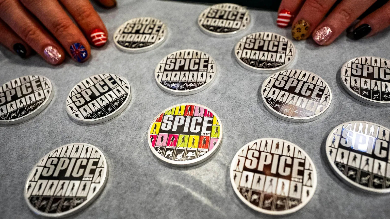 Multiple of the coloured coin laid out on a surface. it features all five members: Victoria Beckham, Melanie Chisholm, Emma Bunton, Geri Halliwell-Horner and Melanie Brown - captured in a silhouette alongside their autographs.