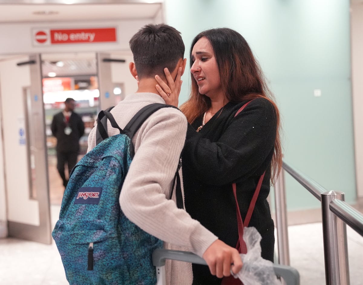 A 12-year-old boy in a light sweater, wearing a blue Jansport backpack, faces away from the camera while a woman with long dark hair holds his face.