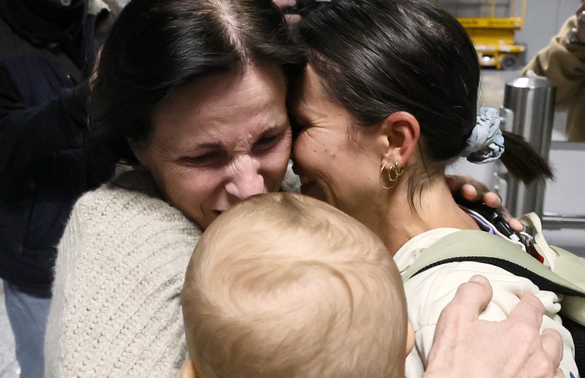 A smiling woman embraces a younger smiling woman holding a baby.