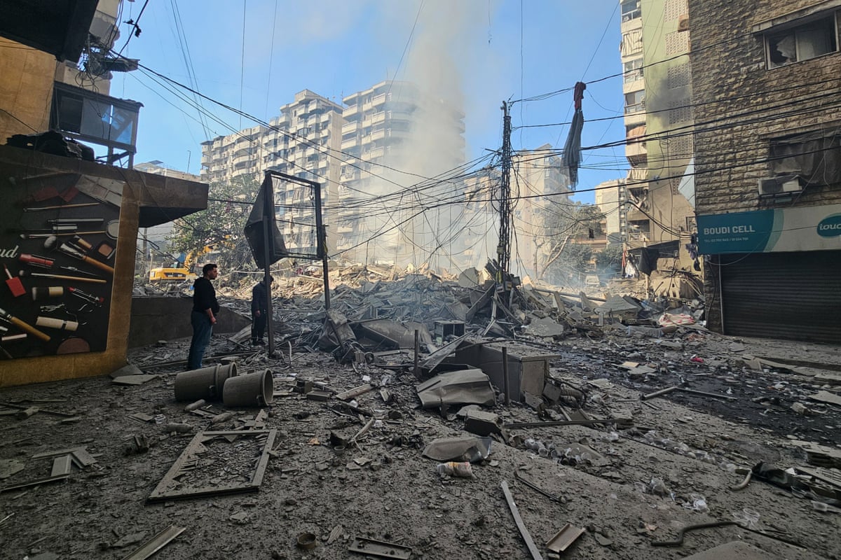 Two people stand amongst debris, dust rising behind them against a blue sky.