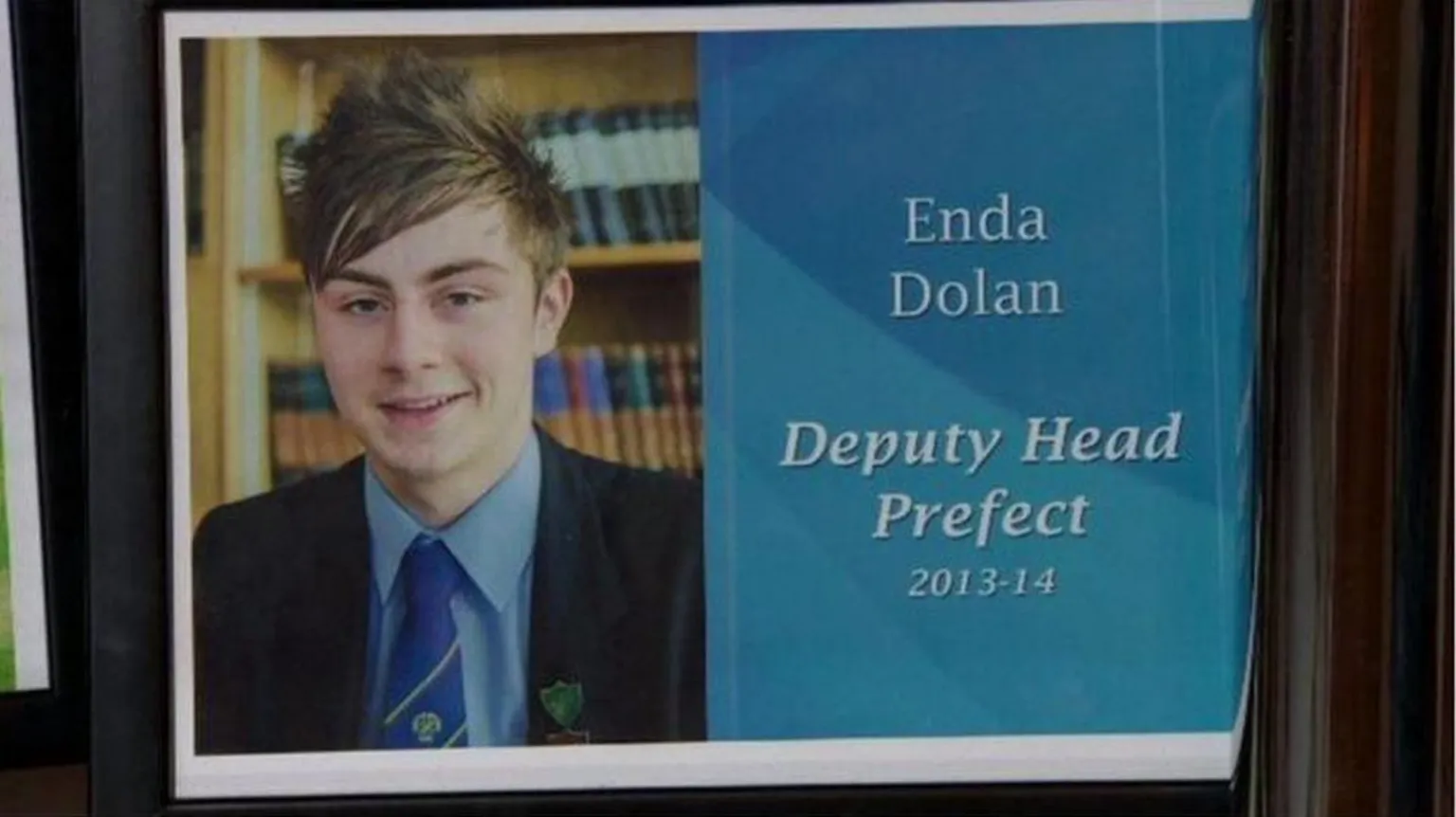 Dolan family A school photo of the late Enda Dolan. He is smiling and wearing a dark school blazer, blue shirt and school tie. The screen is split down the middle and on the other side there is a white graphic on a blue background which reads: 