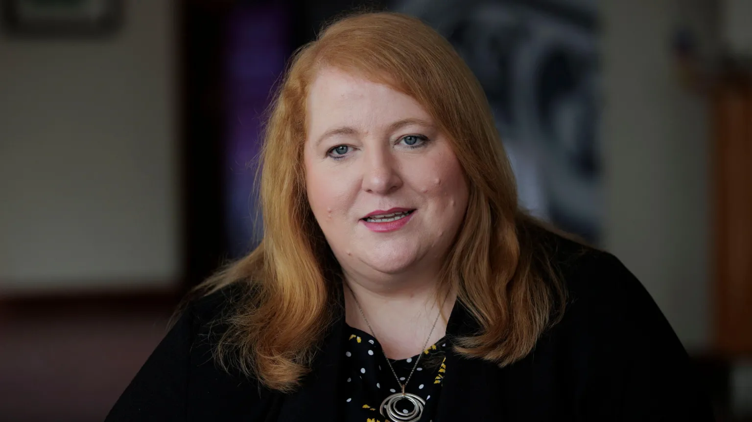 Liam McBurney/PA Wire Justice Minister Naomi Long looking to camera, wearing a black jacket, a black, white and yellow top with polka dots and floral patterns, and a necklace with concentric rings. 