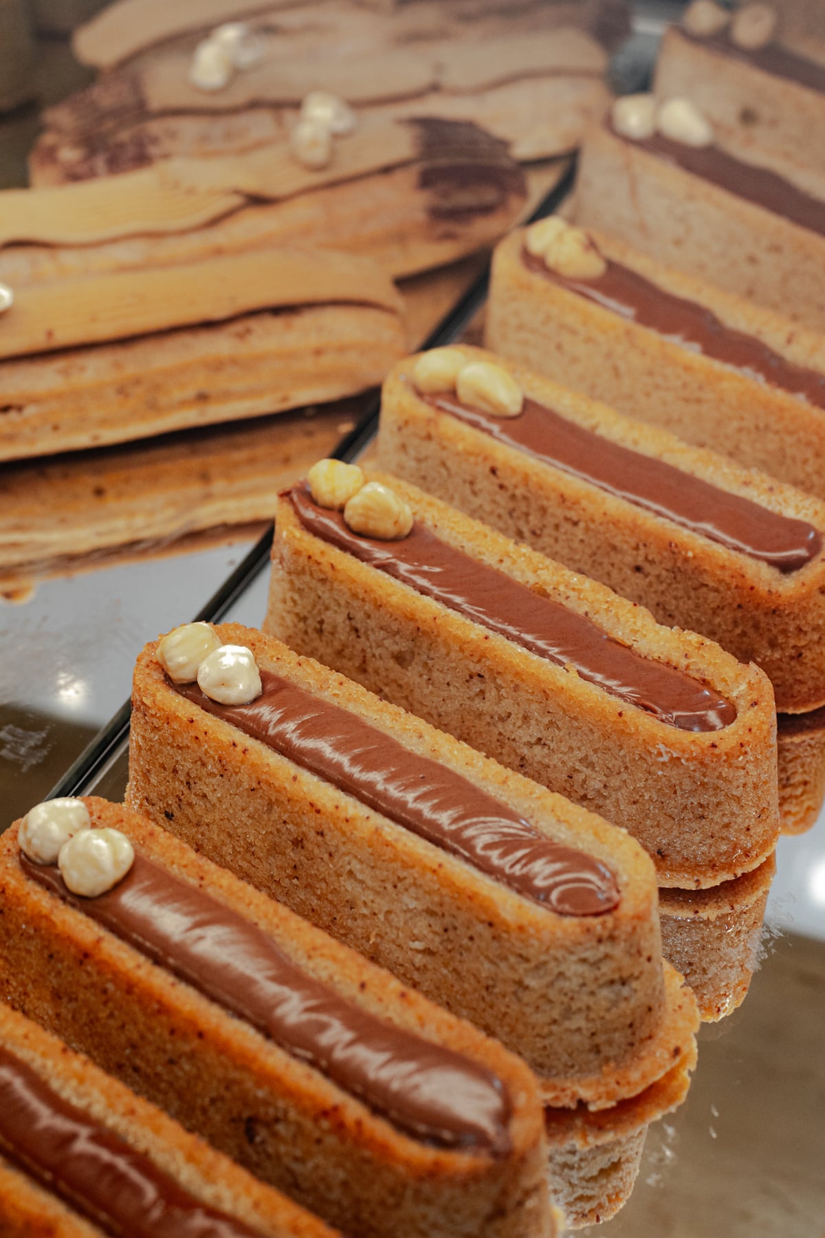 A row of almost-identical financiers covered in chocolate on a glass shelf