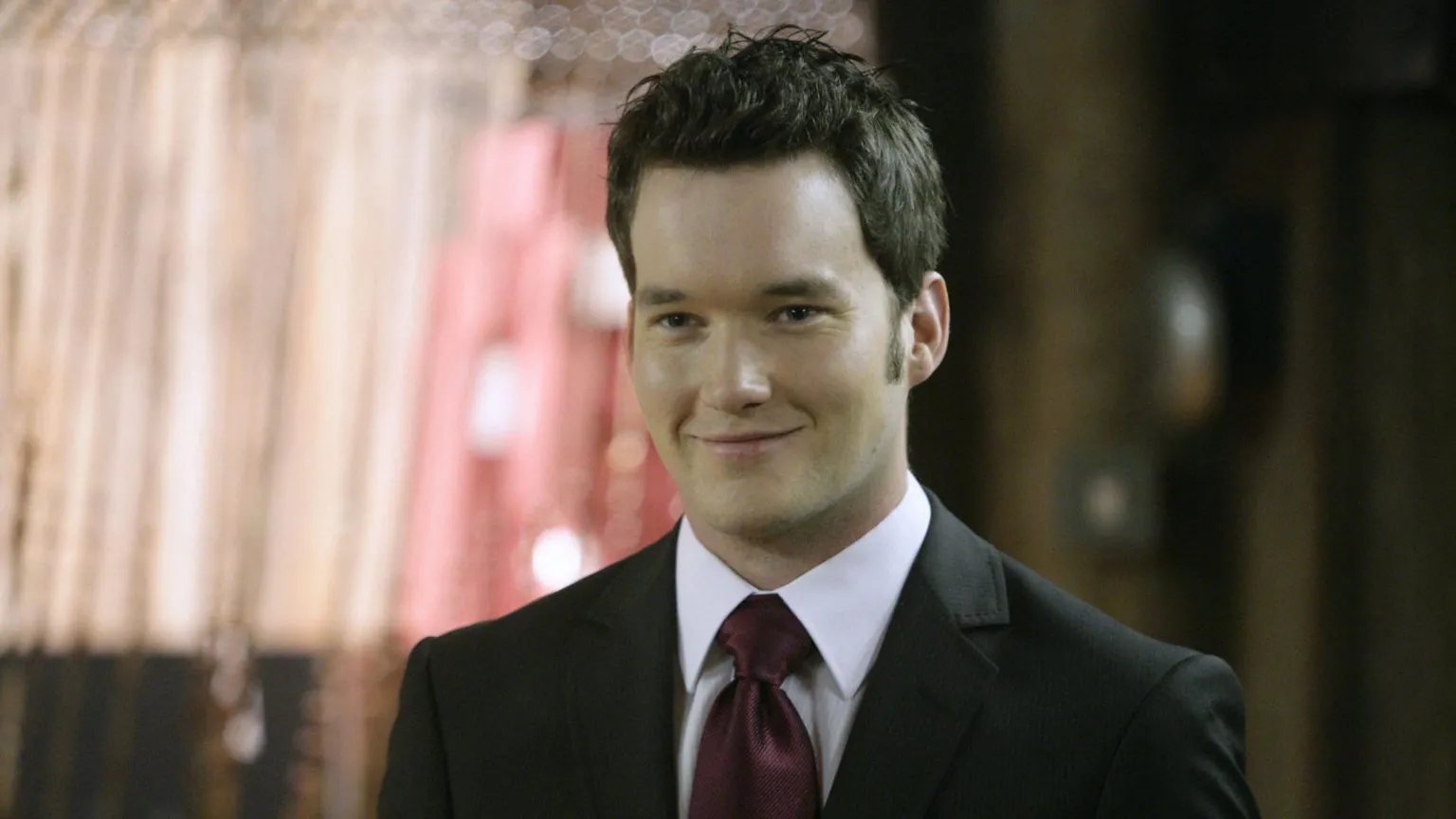 Lloyd wears a black suit with maroon tie.