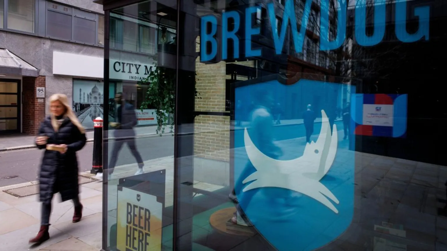  A woman walks past a Brewdog pub, which has the firm's name and logo in the window.