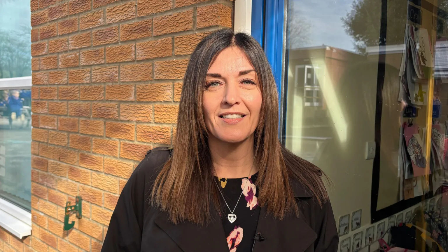 Headteacher of Warter Primary School in York, Helen Houghton smiles into the camera. She's stood outside against a brick wall and is smiling with brunette long hair.