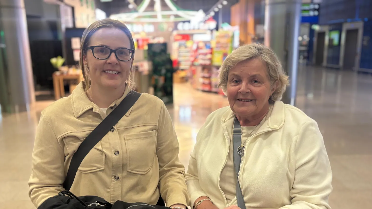 Susan and Monica standing beside each other. Susan has brown hair tied back and a white jacket. Susan has short blonde hair and is wearing a white top and jacket.