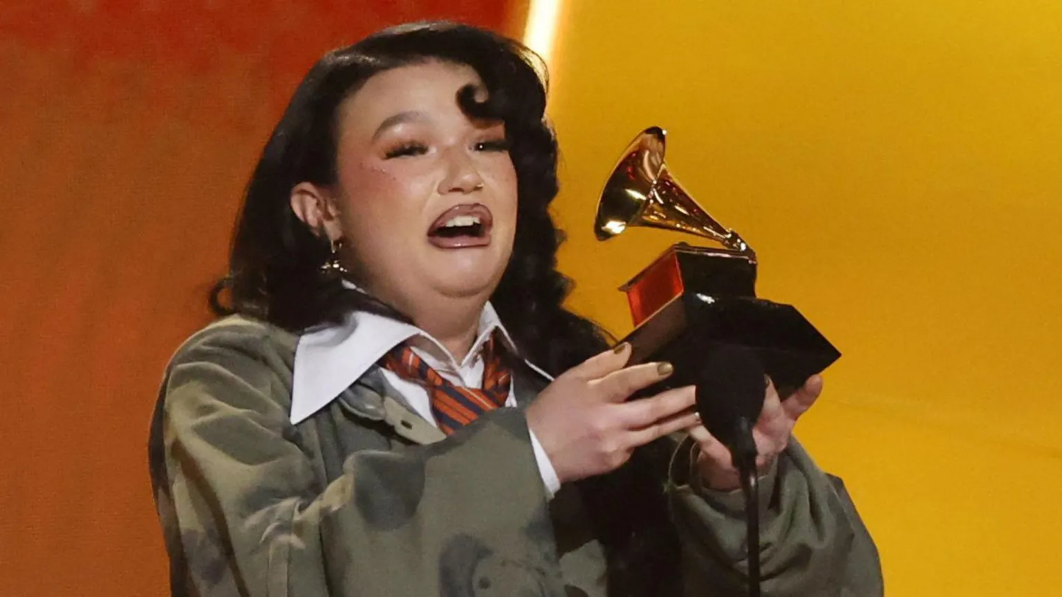  Lola Young on stage at the Grammys, holding up her trophy and giving her speech with an emotional expression