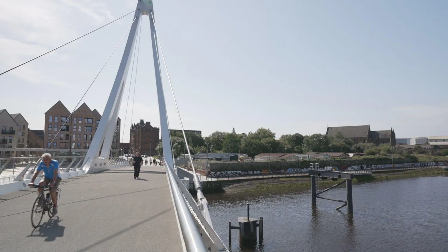 The view from the new Govan Bridge across to the area where the showpeople yard is. There are modern flats on the left of the bridge and on the right, a wall and low chalets and mobile homes sitting behind a high grafitti-ed wall