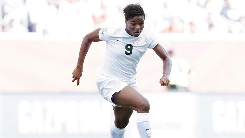 A Nigerian female player in an all-white shirt and short, with number 9 written on it with a green ink, in an action mood on a football field.