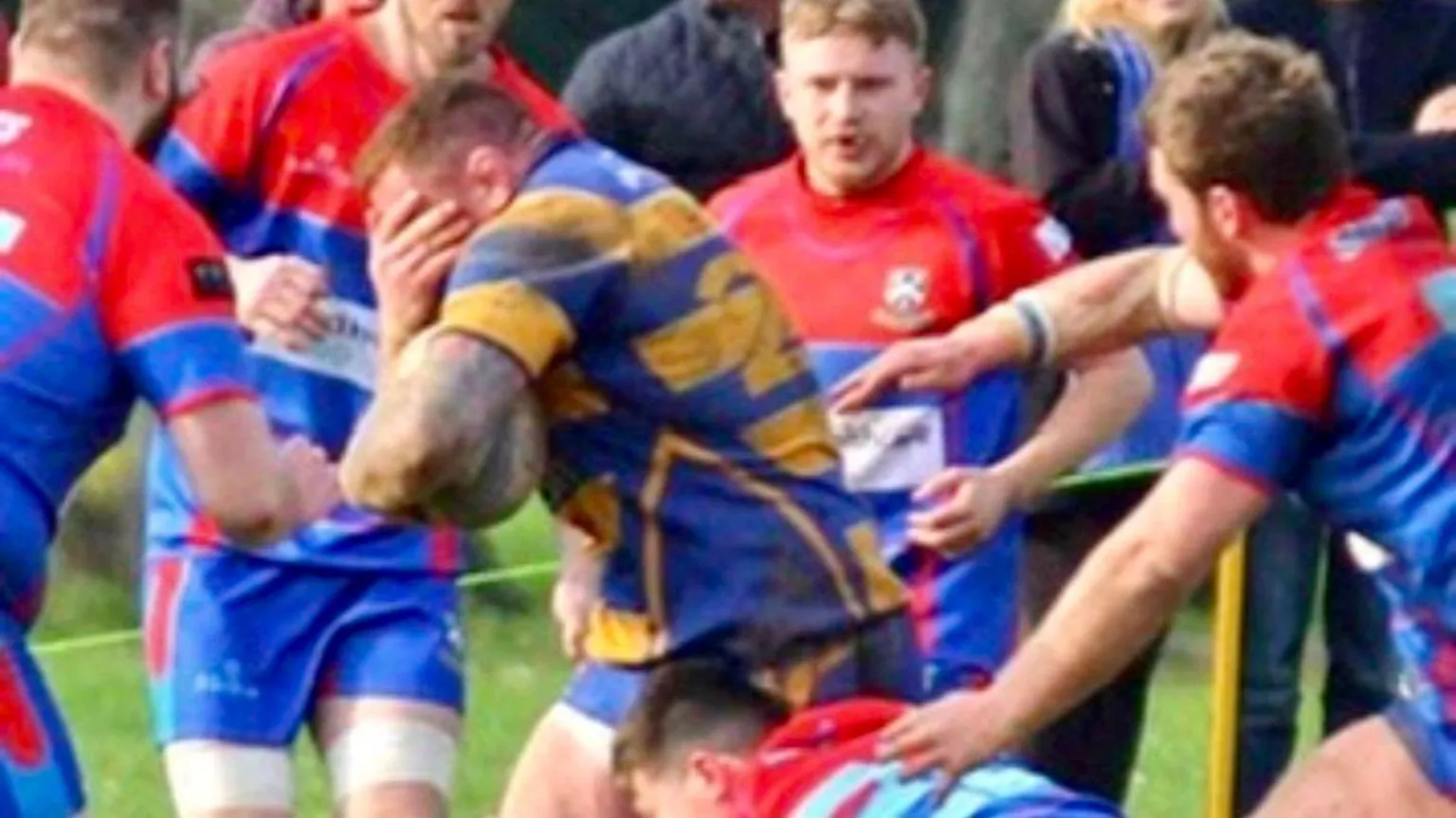 Gareth Roberts Photography Ross is seen playing rugby, surrounded by other players, clutching the ball in one hand and his head in the other.