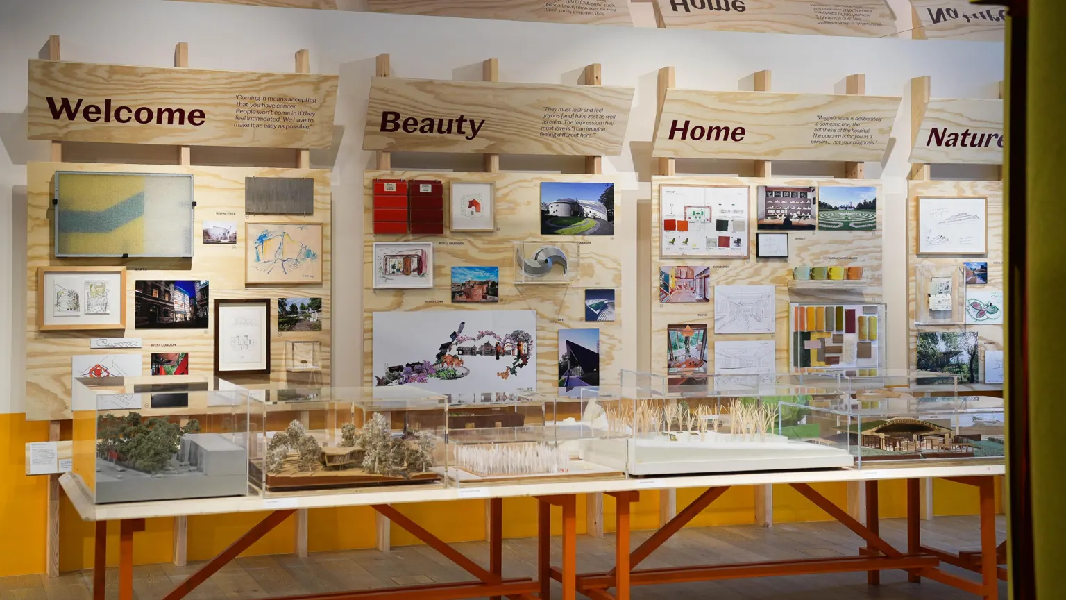 Wall and glass cabinet displays at the Maggie's Exhibition at the V&A Dundee. The cabinets have models of various Maggie's Centre buildings and headings on the wall display say 