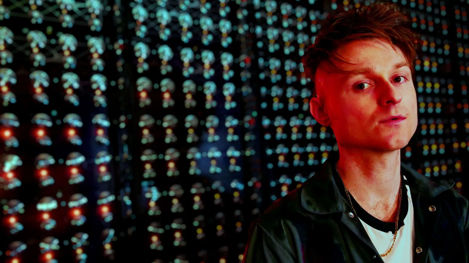 Look Mum No Computer stands in front of his 1,000 Oscillator Drone Synth, bathed in red light