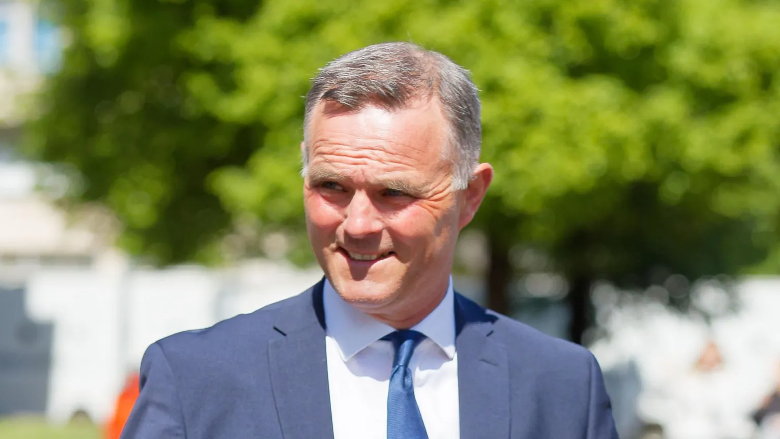 Athena Richard Evan Rhys Williams is pictured leaving Cardiff Crown Court. He is smiling through the sunshine, squinting slightly. He has grey short hair and wears a navy suit, white shirt and navy tie.