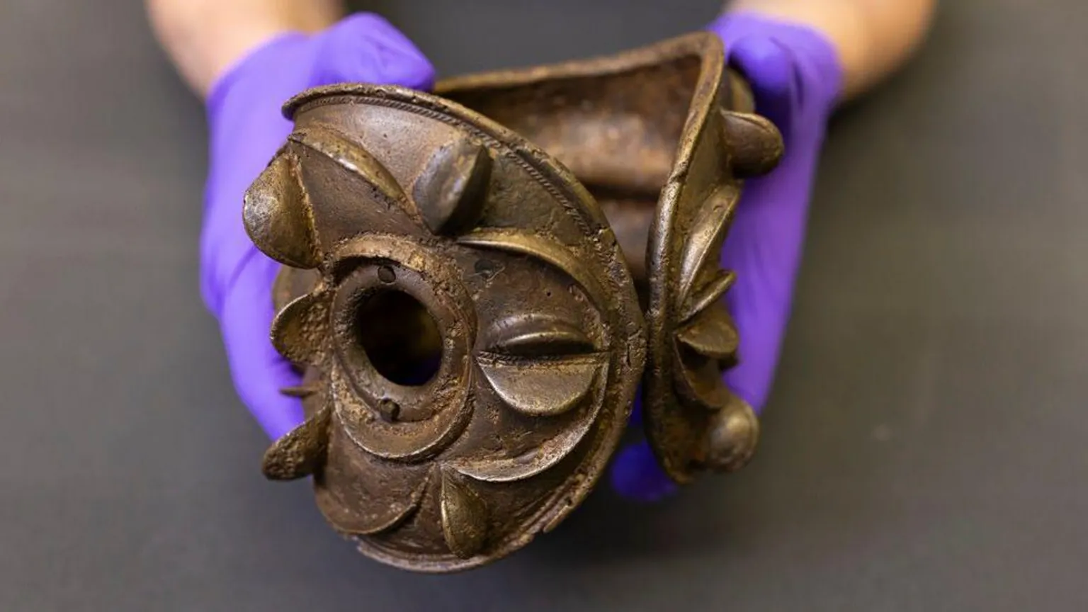 Duncan McGlynn An ornately decorated Iron Age armlet being held by two purple gloved hands