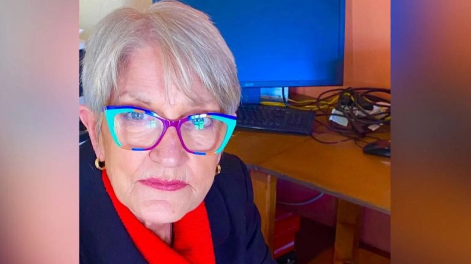 Eilish O'Doherty Eilish O'Doherty has short grey hair and glasses that have multi-coloured frames. She is wearing a dark jacket and red scarf. 